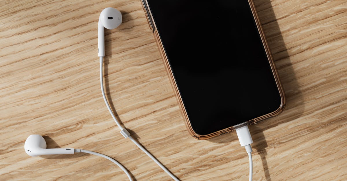 Is it possible to connect with Hainan Airlines from India/Bangladesh? - From above composition of white wired earphones and modern mobile phone with blank screen and connected charging cable placed on wooden surface in daylight