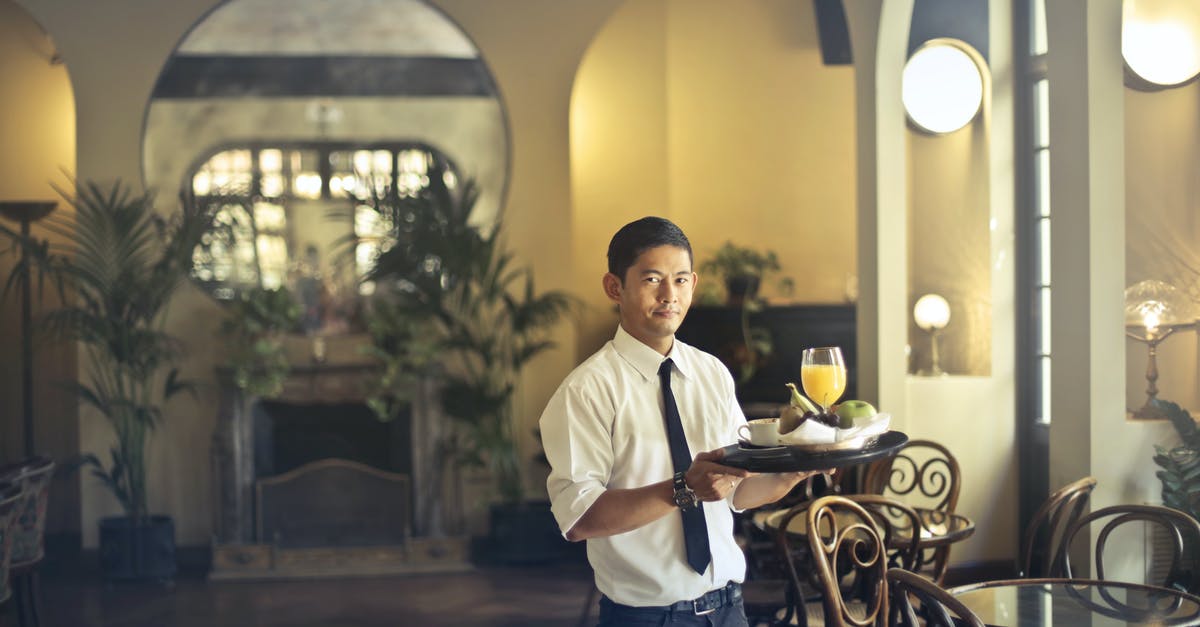 Is it possible to order airag at bars in Mongolia? - Confident young ethnic waiter in elegant clothes holding tray with food and drinks and looking at camera while serving tables in stylish restaurant