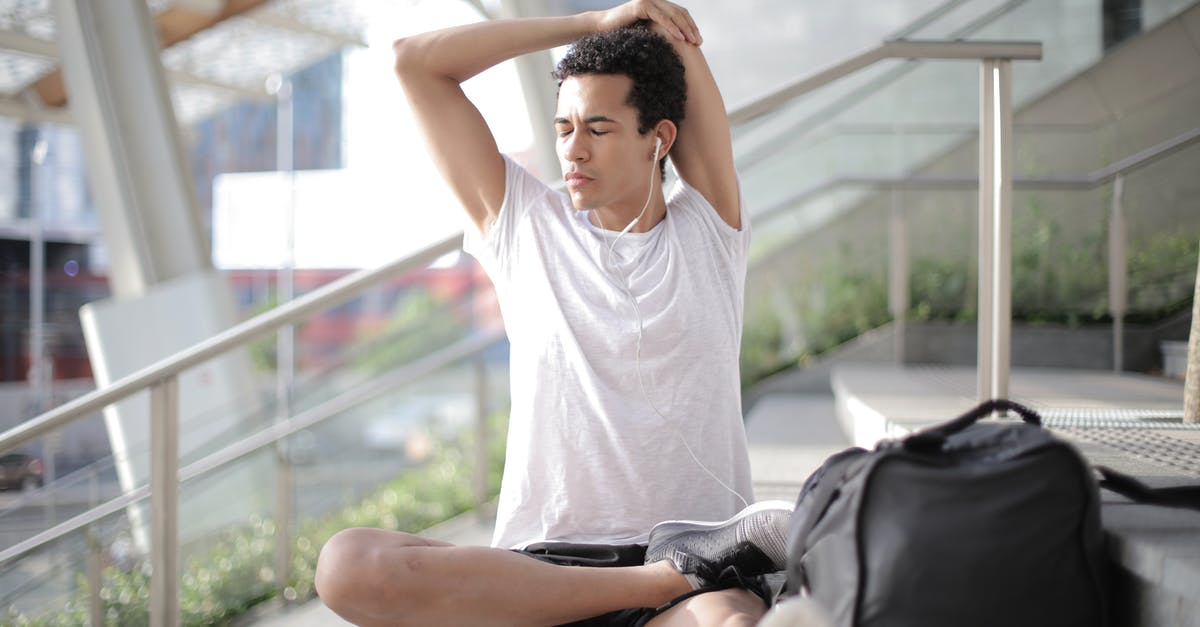 Is it possible to pick up luggage mid-travel? - Young ethnic athlete in earbuds stretching body while sitting on stairs at entrance of contemporary building