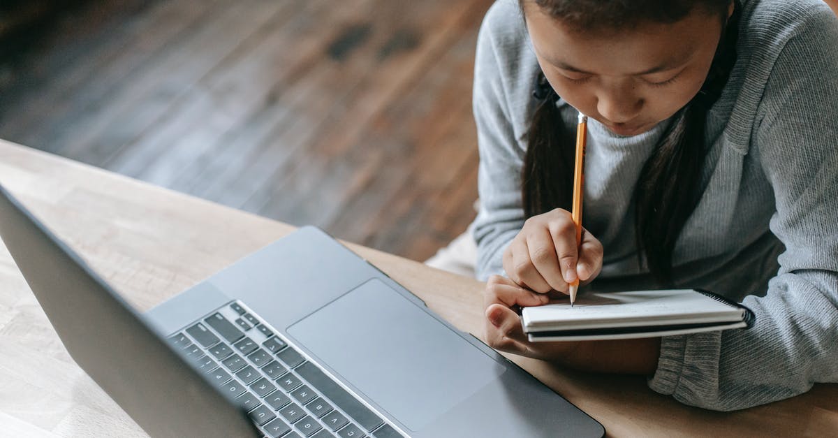 Is it possible to take a desktop PC as carry-on luggage? - From above of crop attentive ethnic schoolchild writing in workbook with pencil while studying at table with netbook