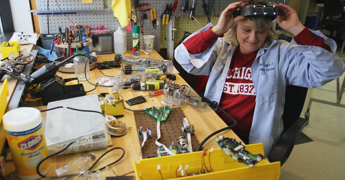 Is it possible to take a soldering iron aboard an airplane? - From above of cheerful female worker in headband magnifier glasses sitting at table with assorted tools and microchips while looking down