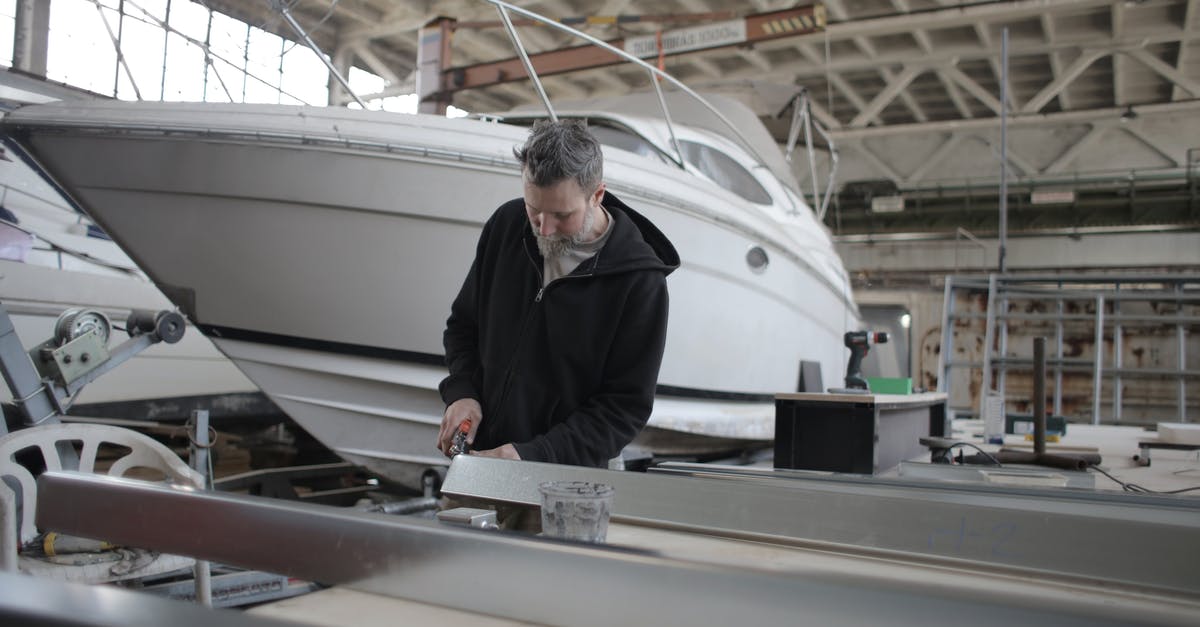 Is it possible to take a soldering iron aboard an airplane? - Concentrated bearded adult workman in casual wear working with metal detail near boat in garage