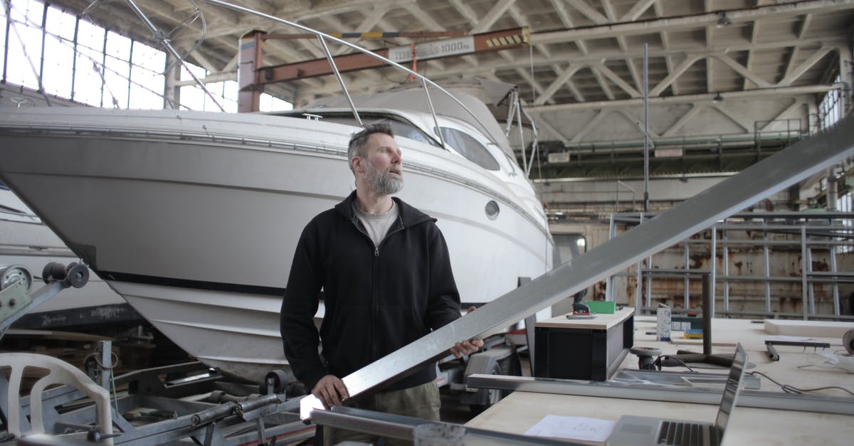 Is it possible to take a soldering iron aboard an airplane? - Side view of adult bearded workman in casual clothes standing near workbench and controlling metal detail in garage with yachts