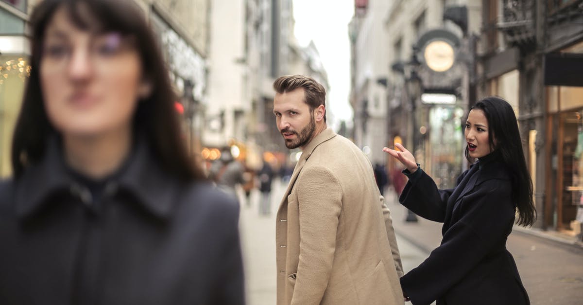 Is it risky to wear a name tag in public in an unfamiliar city? - Man in Beige Coat Standing Near Woman in Black Coat