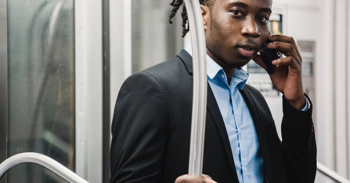 Is it rude to talk on a mobile phone for the whole journey, when travelling alone in a London black taxi? - Young handsome African American male in formal suit making phone call on smartphone while traveling by commuter train