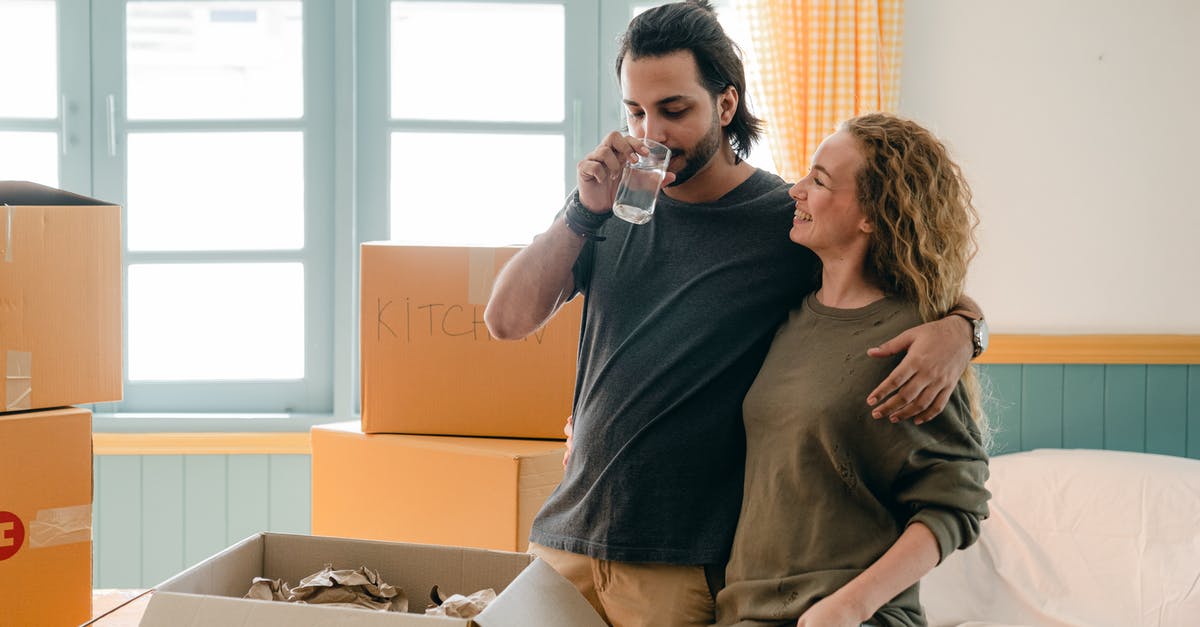 Is it safe to drink tap water in New Zealand? - Cheerful multiethnic couple embracing while drinking water near different boxes