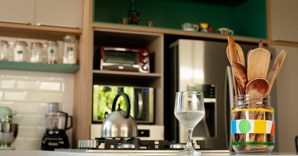 Is it safe to drink tap water in New Zealand? - Glass of cold water and wooden utensils in jar placed on counter near stove with kettle in cozy kitchen with modern appliances