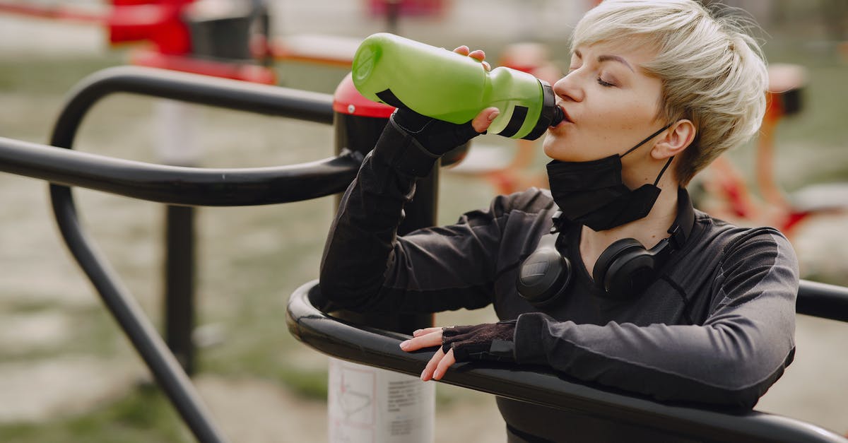 Is it safe to drink tap water in Seoul? - Calm female in sportswear and sport gloves with headphones on neck leaning on street exercise machine  drinking water from plastic bottle