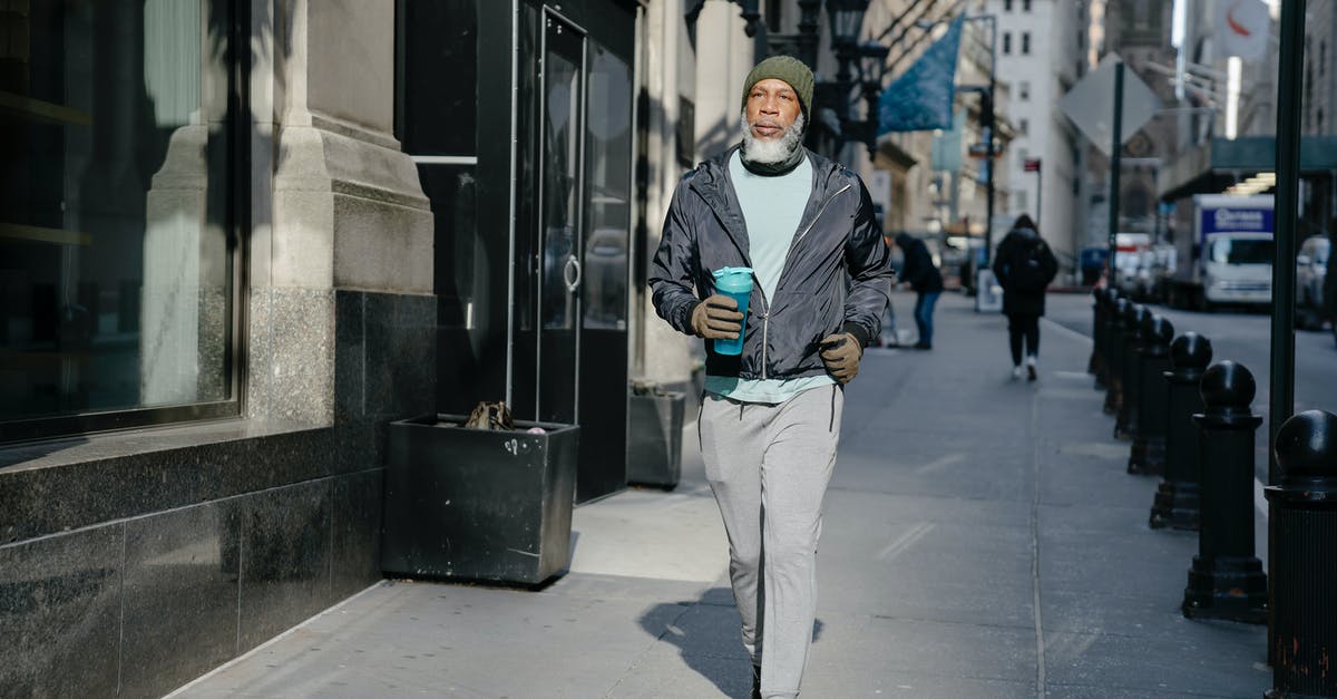 Is it safe to drink water with a strong chlorine smell? - Full body of confident bearded African American male in activewear and warm gloves and hat walking along sidewalk with fitness bottle for water in sunny morning