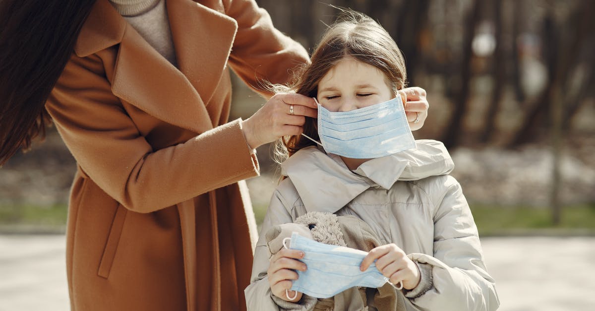 Is it safe to put a PS4 in checked luggage? - Crop female helping to put on medical mask for daughter during stroll in nature