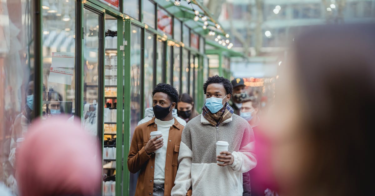 Is it safe to roller-skate on sidewalks in USA? - African American homosexual male in protective masks holding hands while strolling on street with takeaway coffee on street with people