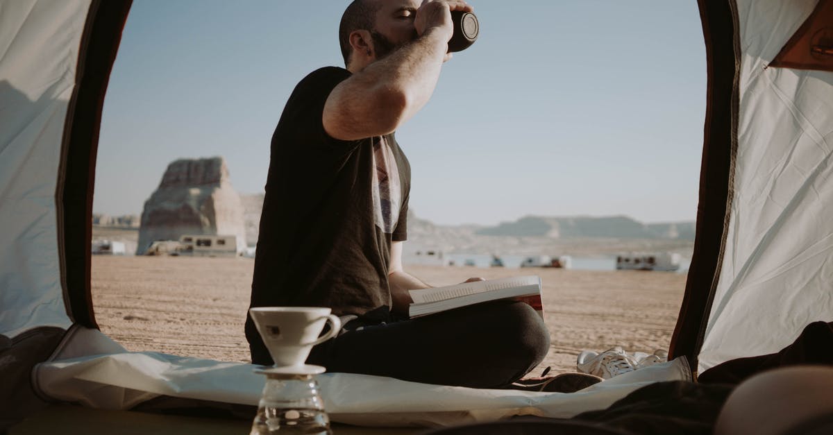 Is Khasan open to tourists? - Side view of male traveler sitting in tent with book near pour over cup while drinking hot beverage in nature during trip