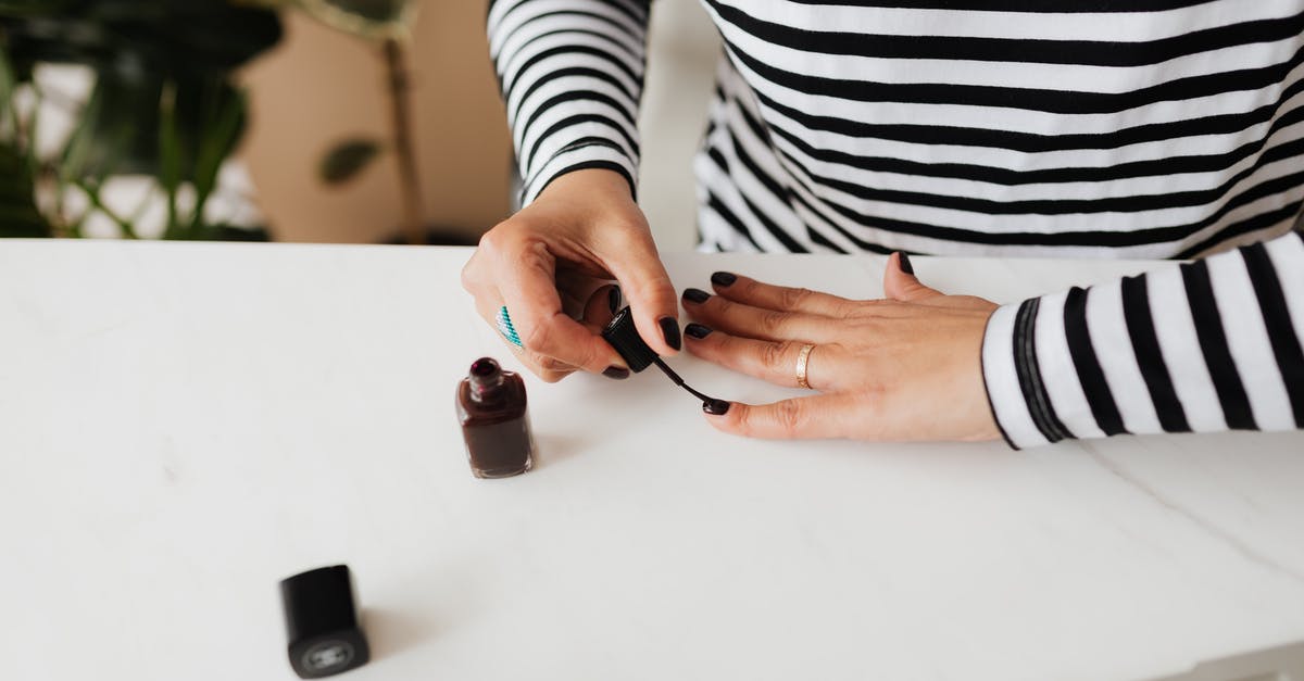 Is nail polish and / or nail polish remover prohibited? - Unrecognizable female doing manicure with black nail polish on white table resting at home during weekend