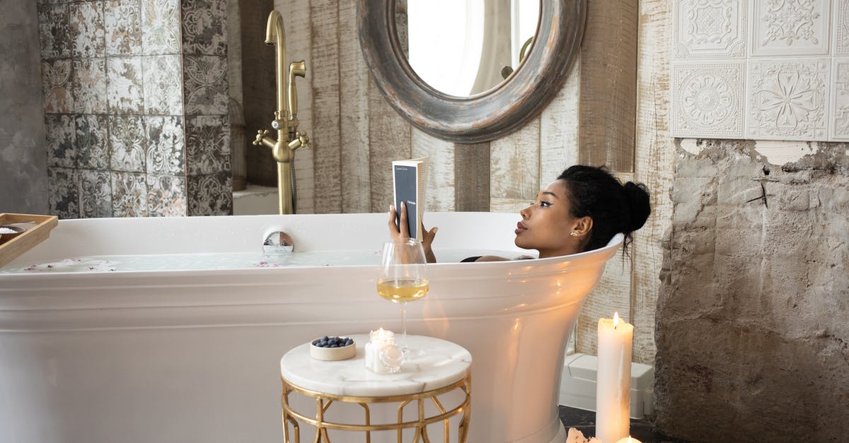 Is tap water drinkable in Massachusetts (and elsewhere in USA)? - Side view of young African American female reading book while lying in bathtub and enjoying spa procedure with wine glass on small marble table and aroma candles