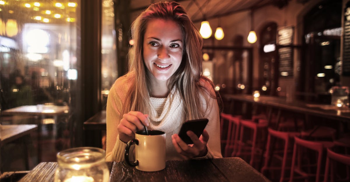 Is tea and coffee on the street safe to drink in India? - Delighted woman with cup of beverage browsing smartphone in cafe