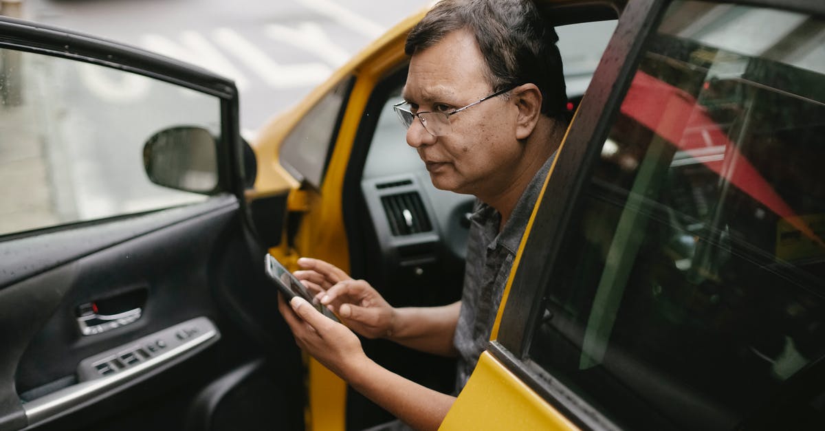 Is the Budapestcard worth the price if I use it for transport mainly? - Crop Asian man sitting in parked yellow taxi car with open door and using smartphone while looking away