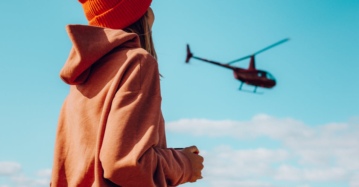 Is the youth price applicable to foreigners for air travel in Scandinavia? - Low angle side view of unrecognizable female traveler in stylish warm outfit looking at helicopter flying in blue sky on sunny day