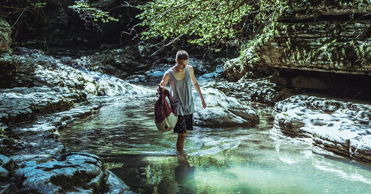 Is there a bag I can use to safely carry my passport and ID whilst travelling? - Man Walking on River in Between Stone and Tree