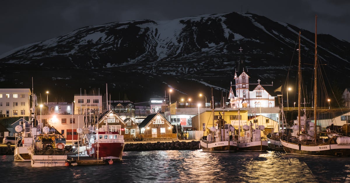Is there a boat that will take tourists to Iceland from North America? - Seafront of brightly lit Husavik harbor late at night in Iceland with sailboats at quayside and dark snow covered mountain in background