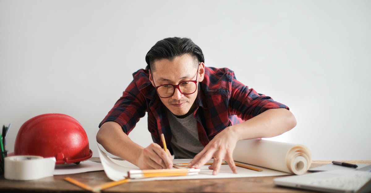 Is there a car-rental scheme that works worldwide? - Inspired young male engineer in glasses drawing draft on paper bending over table against white wall