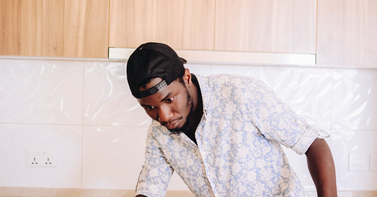 Is there a daily fare cap on the Taipei MRT? - Concentrated African American male in shirt and black cap cleaning surface of table in bright cozy apartment decorated in pastel colors