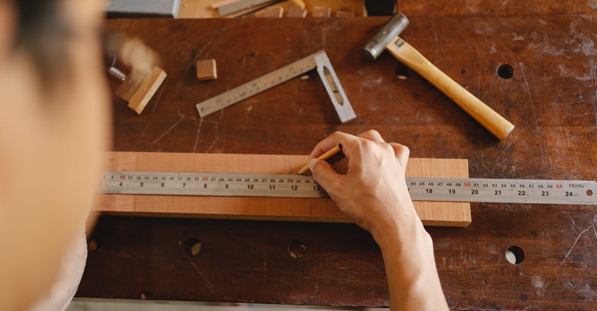 Is there a limit on the number of a single item I can take with me on a plane? - Top view of crop anonymous male measuring timber plank with ruler and marking with pencil while working on table with tools