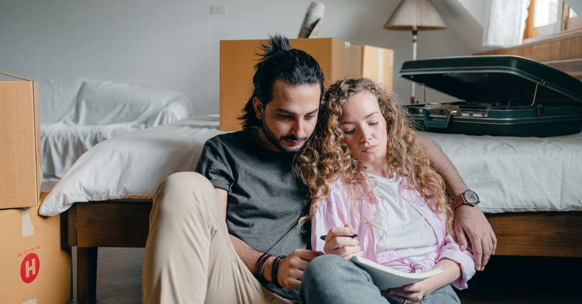 Is there a list of free accommodation resources? - Thoughtful male and female in casual wear sitting near bed among boxes together and taking notes while moving house