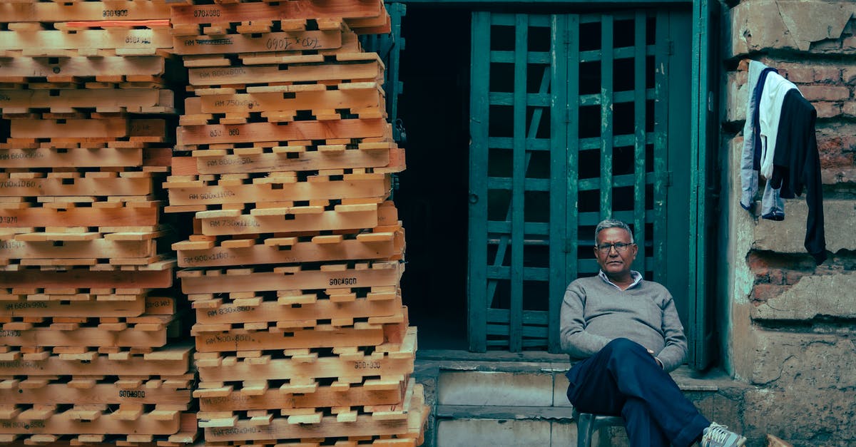 Is there a possibility the company can block my b1/b2 visa? - Man Sitting in Front of a Building with a Stack of Pallets Next to Him 