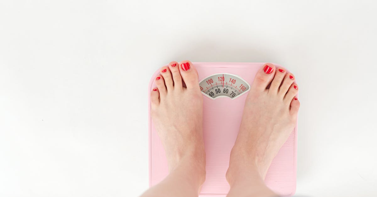 Is there any trick to checking in more weight on planes? - Top view of crop anonymous barefoot female measuring weight on scales on white background