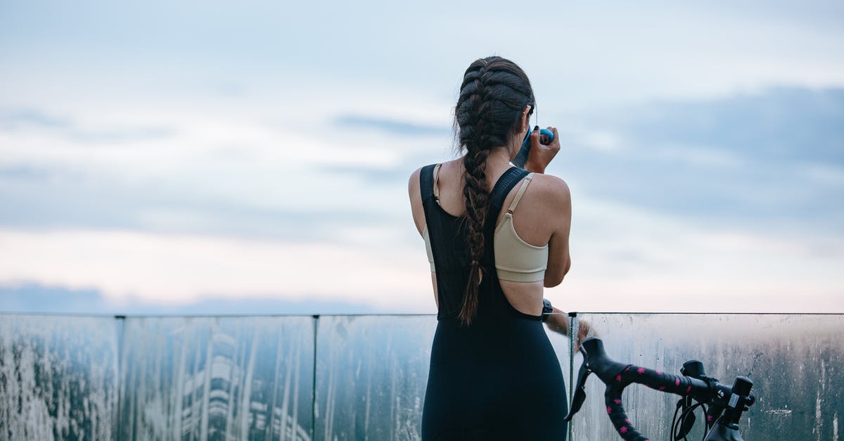 Is there camping gear specifically designed to fit modern air traveling? - Back view of unrecognizable sportswoman drinking beverage from mug near bicycle and fence while having break