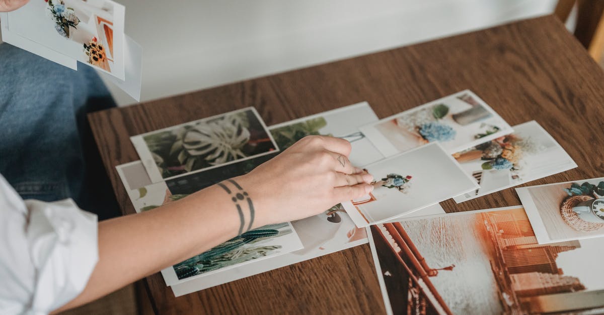 Is this airliner-shaped lake real? - Crop anonymous tattooed female with different photos of flowers and city at desk in house room