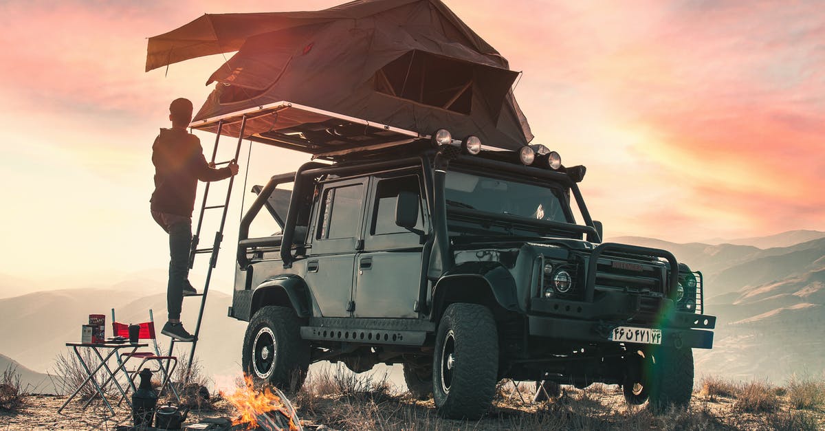 Is wild camping allowed in Norway? - Back view of crop anonymous male traveler watching sunset during camping in mountains and climbing upstairs to tent located on roof of contemporary offroader