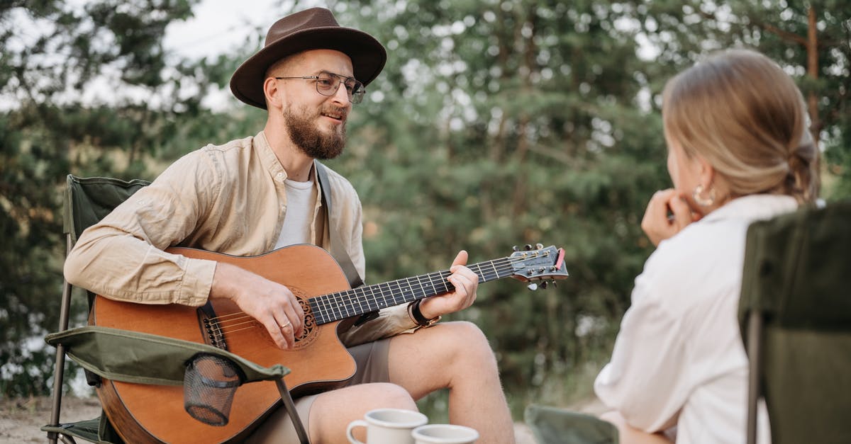 Isle of Man Camping (IOM TT Specific) - A Bearded Man Playing Guitar while Looking at the Woman Sitting in Front of Him