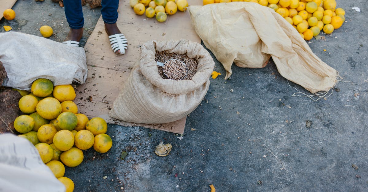 It is cheaper to buy the whole trip or leg by leg? - From above of crop faceless seller near pile of ripe oranges on ground and bag of grains at bazaar