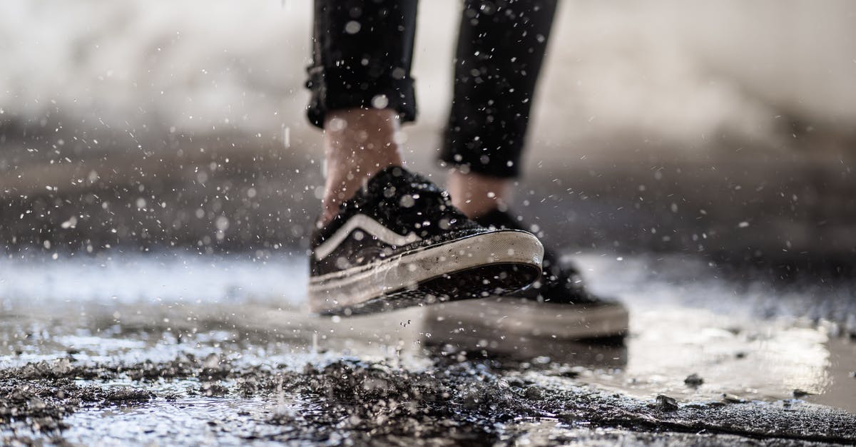 It is cheaper to buy the whole trip or leg by leg? - Crop person walking through puddles on asphalt