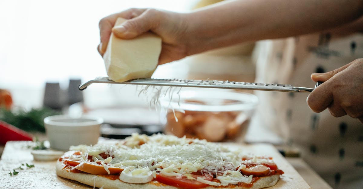 Italian consulate Schengen visa time - Side view of crop unrecognizable person grating piece of hard cheese on palatable homemade pizza in kitchen at daytime