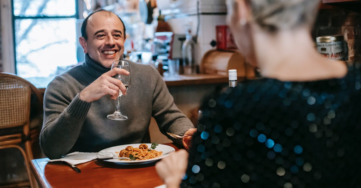 Italian Visa has wrong dates - Couple sitting at table while having dinner with pasta with meatballs on plate with glass in light room with chairs near window