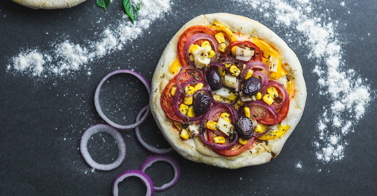 Japanese Corn and Mayo Pizza - Flat lay of pizza with sliced onion and tomatoes covered with corns on table with flour and green leaves