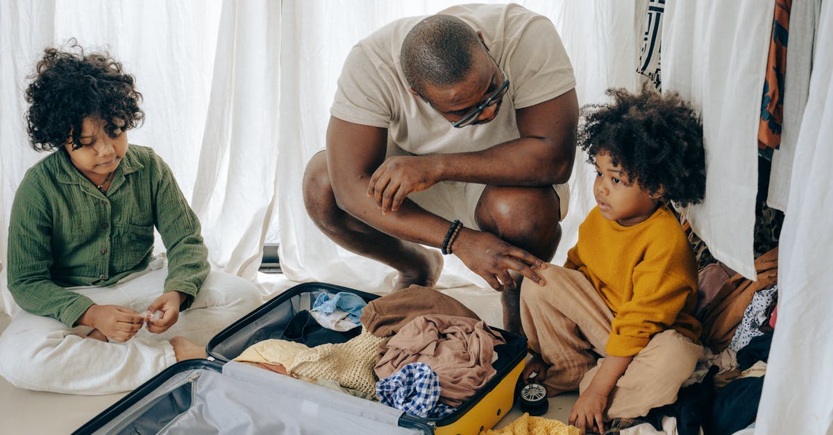 JFK International to Domestic Baggage Drop - African American father in eyewear with sad kids with curly hair sitting near opened suitcase