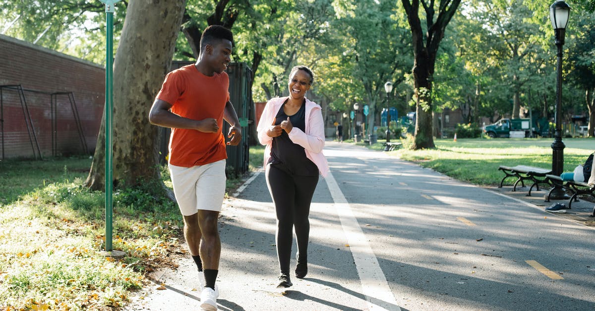 Jogging in Bucharest? - Man in White Tank Top and Black Pants Holding a Phone Walking on the Street during