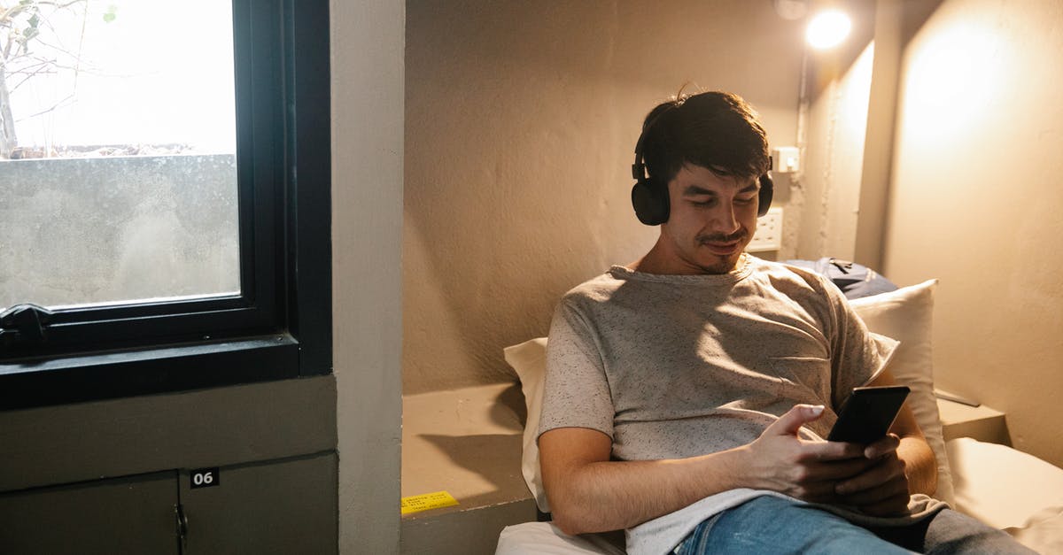 Journey planner for finding intercity train connections in China? - Smiling man resting on bed and using smartphone and headphones