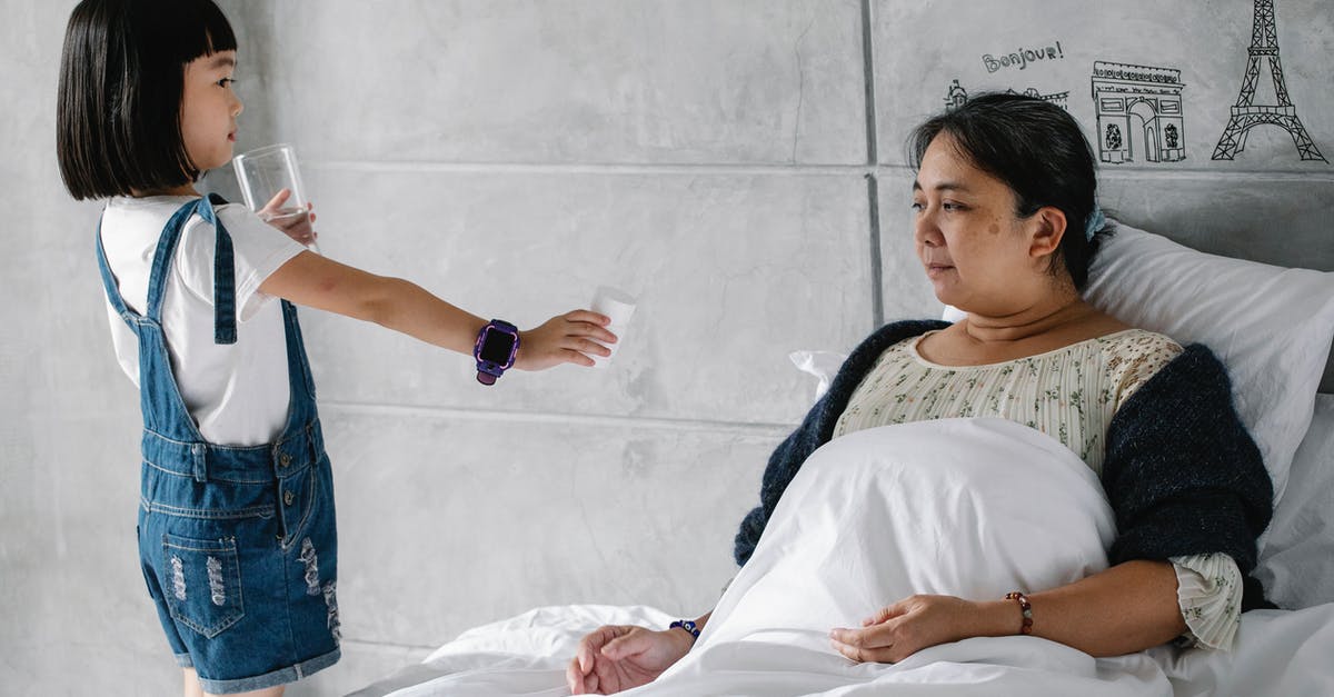 Just what is unhealthy in the water in Mexico? - Side view of adorable little Asian girl giving medicine and water to sick grandmother sitting in bed