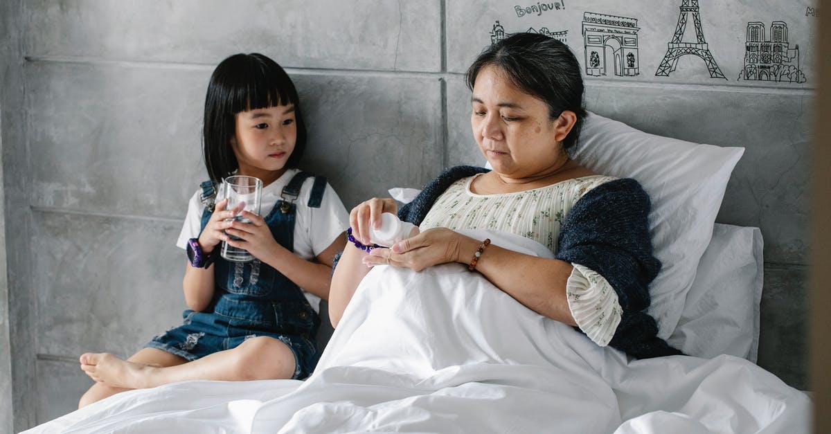 Just what is unhealthy in the water in Mexico? - Focused little Asian girl sitting on bed near sick grandmother drinking pills