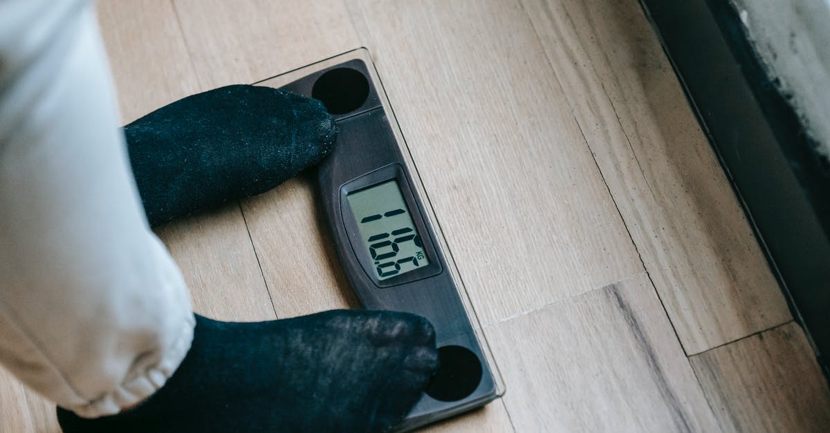 KLM carry-on weighing precedent? - From above of unrecognizable person in socks standing on electronic weighing scales while checking weight on parquet during weight loss