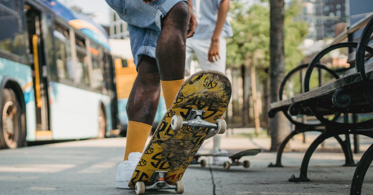 Krakow MDA Bus stop - tickets to Busko Zdroj [closed] - Crop unrecognizable male in yellow socks standing on colorful skateboard tail and deck at angle with friend while waiting for bus on bus stop