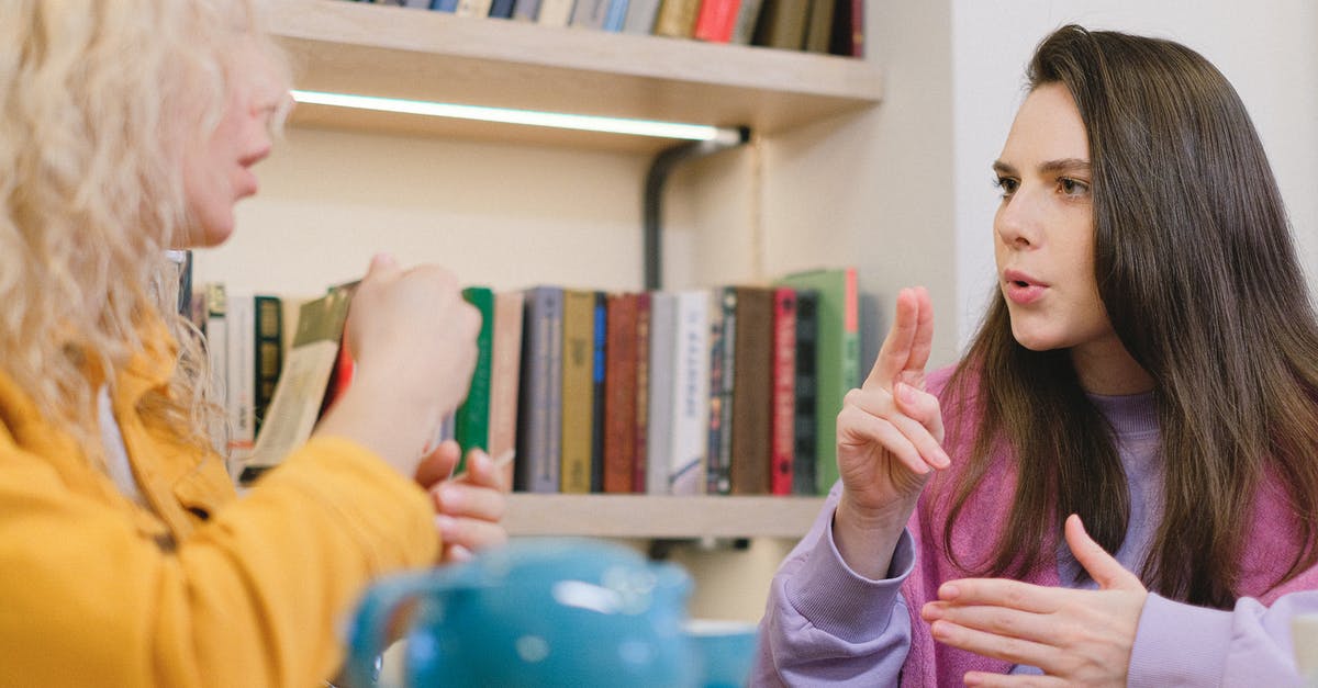 Language to communicate in tourist places in Bratislava? English is sufficient? - Side view of female friends sitting at table in university library and using sign language