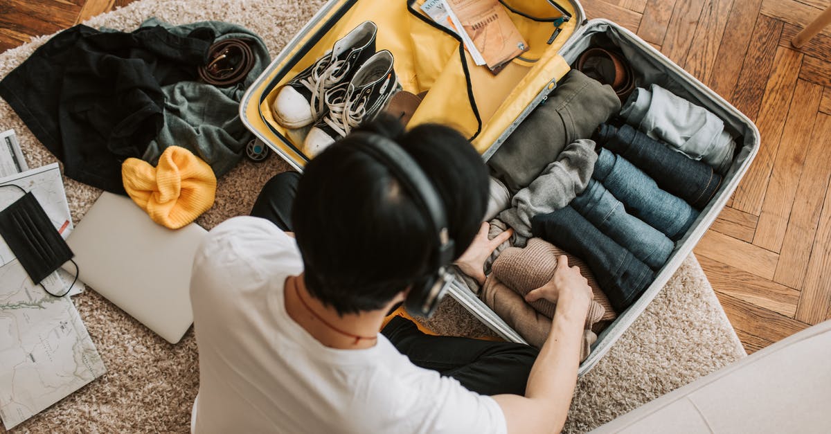 Laptop in a suitcase - A Man Listening on His Headphones while Packing His Clothes