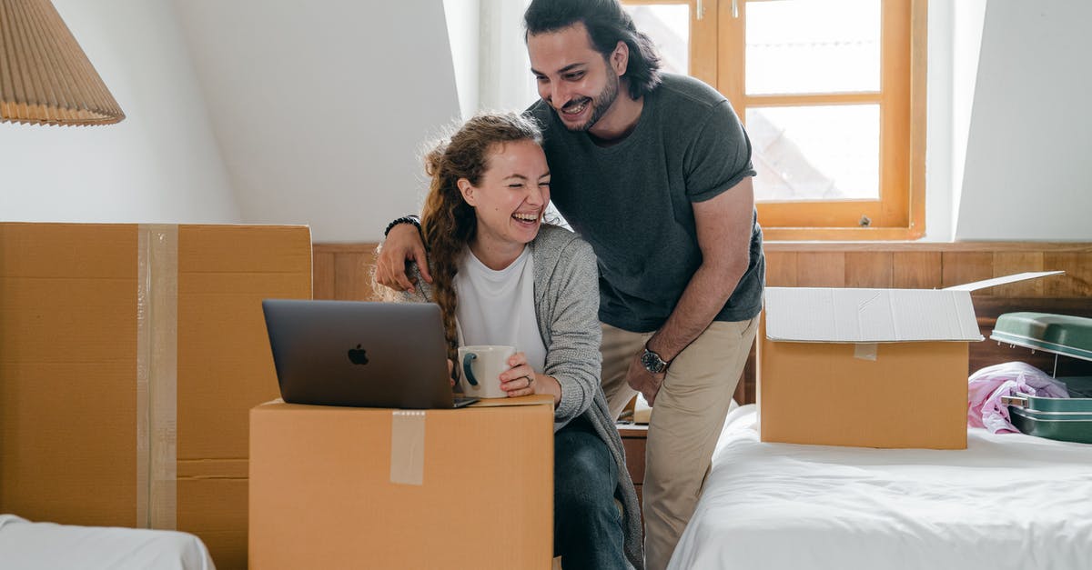 Laptop in a suitcase - Happy diverse couple with laptop sitting in attic style bedroom