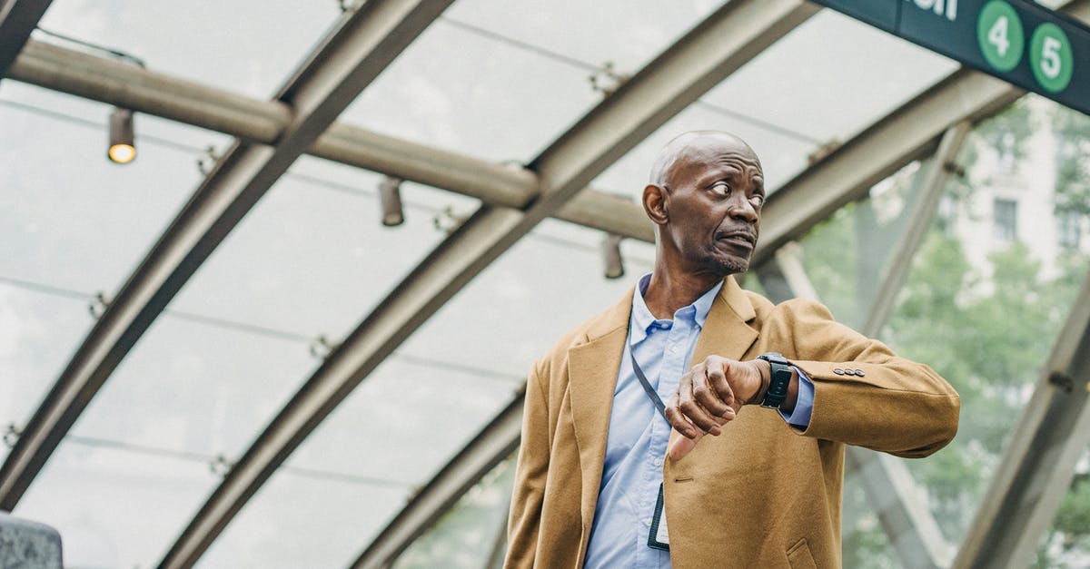 Late Check In rules - Serious African American businessman in formal clothes standing in subway station and checking time on wristwatch while looking away thoughtfully