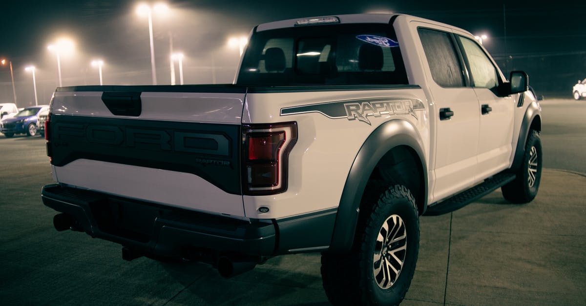 Late night transportation in Leipzig - White pickup truck on parking lot with cars under shiny streetlamps at night